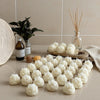 White lotus flower-shaped candles arranged in rows on a beige surface with reed diffuser and bottles in background.