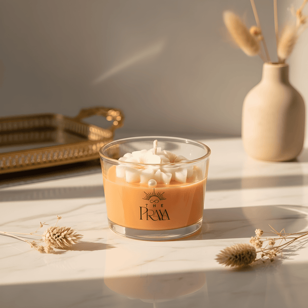 Orange blossom scented candle in clear glass jar with floral-shaped white wax top and black logo.
