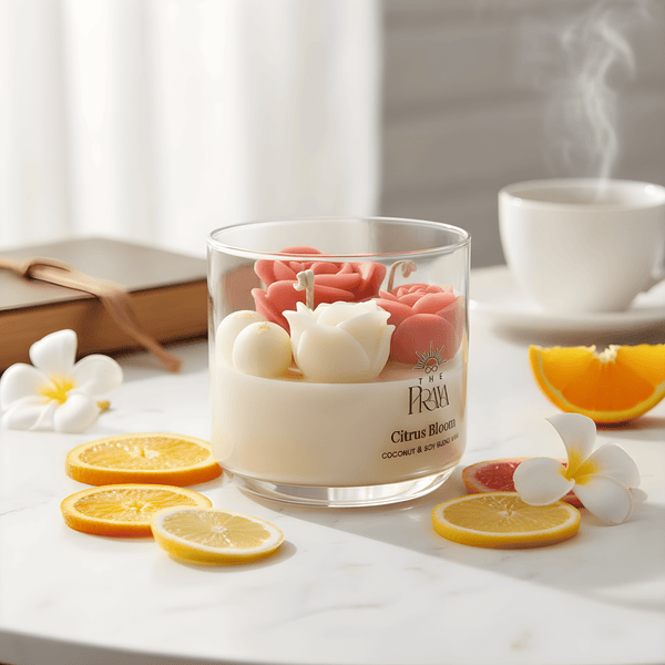 Clear glass jar candle with three wicks and decorative pink and white rose-shaped wax flowers, placed on a marble surface.