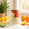 3-wick jar candle labeled Citrus Bloom with coconut and soy blend, surrounded by citrus fruits.