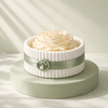 White ceramic jar with ribbed texture and green ribbon, holding cream-colored flower-shaped candle.
