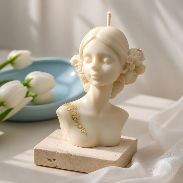 Cream-colored lady bust candle with floral hair details on a square stone base.