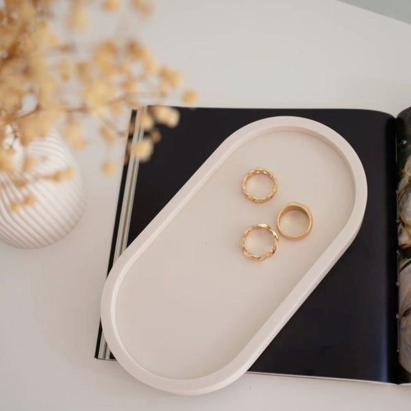 Beige oval tray holding three gold rings on an open black and white book background.