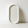 Minimalist white oval tray with raised edges on a textured surface against a plain wall.