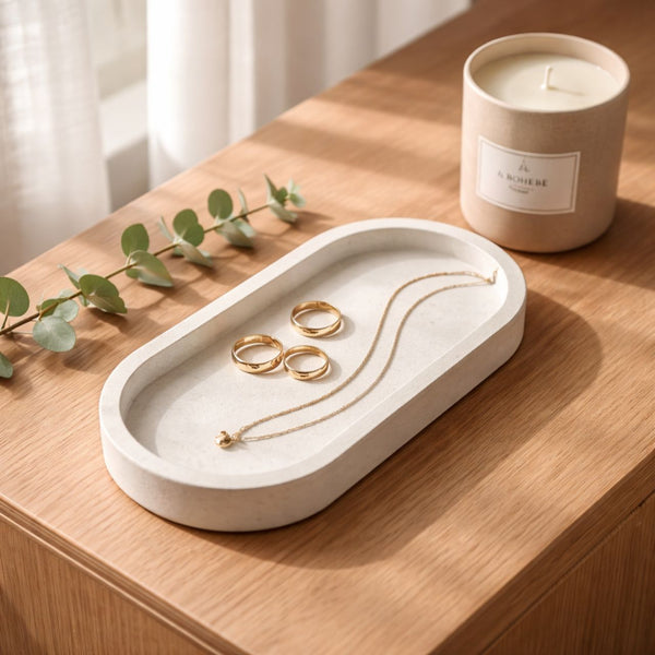 Oval white marble tray holding gold rings and a delicate gold necklace on wooden table.