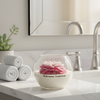 Round glass jar candle with layered pink peony flower wax and white base labeled Mahogany Teakwood on marble bathroom.