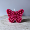 Pink butterfly-shaped candle with detailed cutout wing patterns and a centered wick.