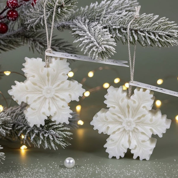 White snowflake-shaped candles hanging on frosted pine branches with warm fairy lights background.