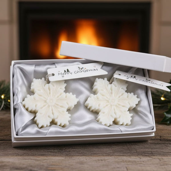 White snowflake-shaped candles in a satin-lined gift box with a white lid and Christmas tags.