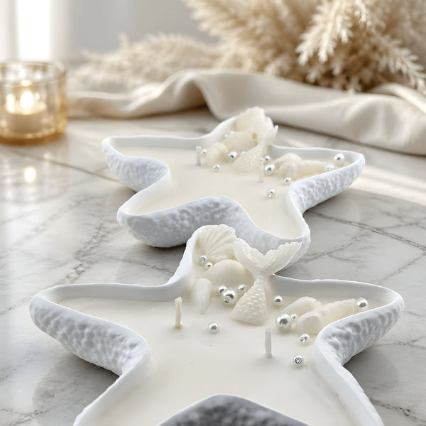 White starfish-shaped candles with textured edges on a marble surface, adorned with small decorative pearls and seashells.