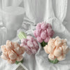 Set of four tulip-shaped candles in soft pink and peach tones with green stems on white fabric background.