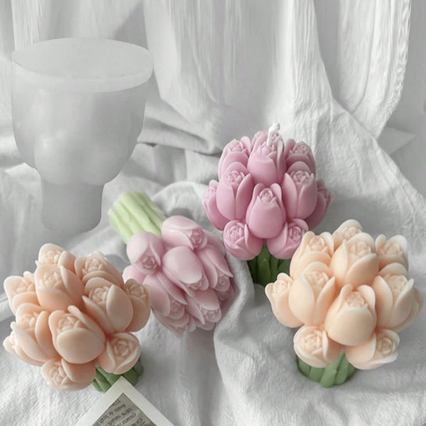 Set of four tulip-shaped candles in soft pink and peach tones with green stems on white fabric background.