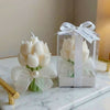 White tulip-shaped candle with green leaves, pearl accent, and sheer bow gift boxed with ribbon and tag.