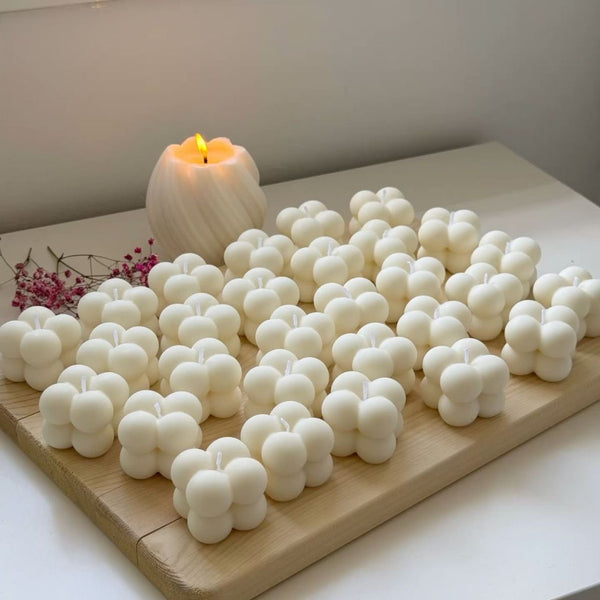 Set of ten white bubble candles arranged on a wooden board with a lit white candle in the background.