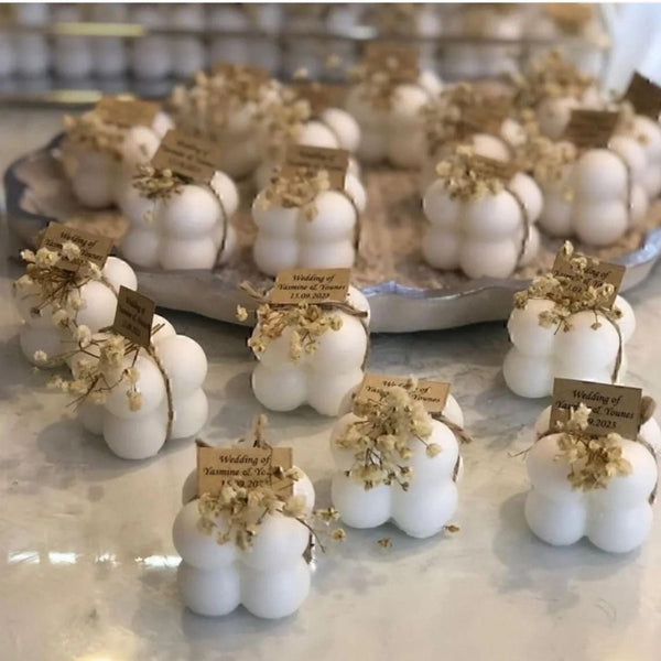 Set of white bubble candles with dried flower accents and rustic tags arranged on a tray and marble surface.