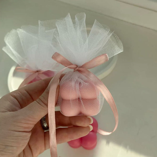 Hand holding a pale pink bubble candle tied with sheer white fabric and a pink satin ribbon.