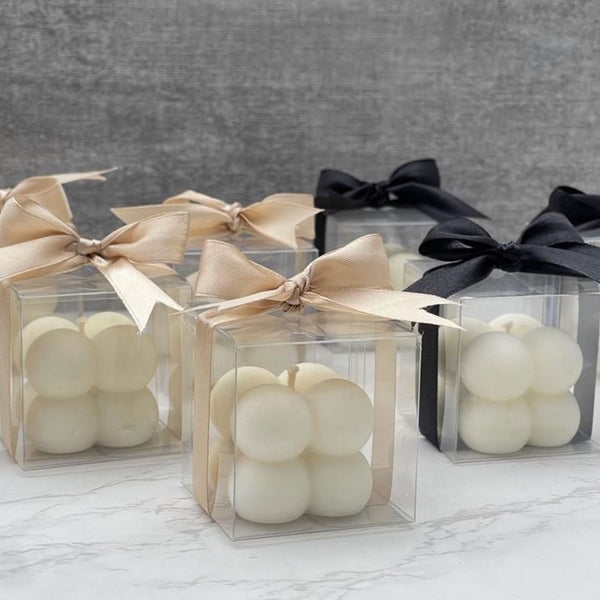 Set of 10 cream and black bubble candles in clear boxes with matching satin bows on marble surface.