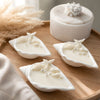 Three white conch shell-shaped soy wax candles with starfish and pearl details on a round wooden tray.