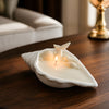 White conch shell-shaped soy wax candle with two lit wicks on wooden table.