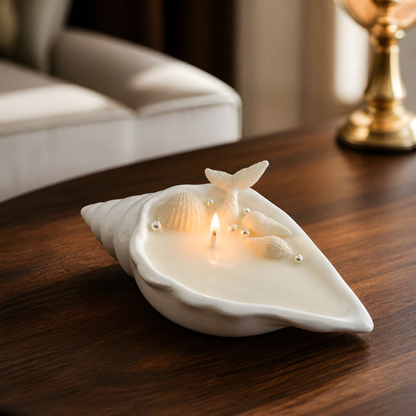 White conch shell-shaped soy wax candle with two lit wicks on wooden table.
