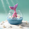 Round glass jar candle with blue wax, white seashell decorations, and a pink mermaid tail wick.