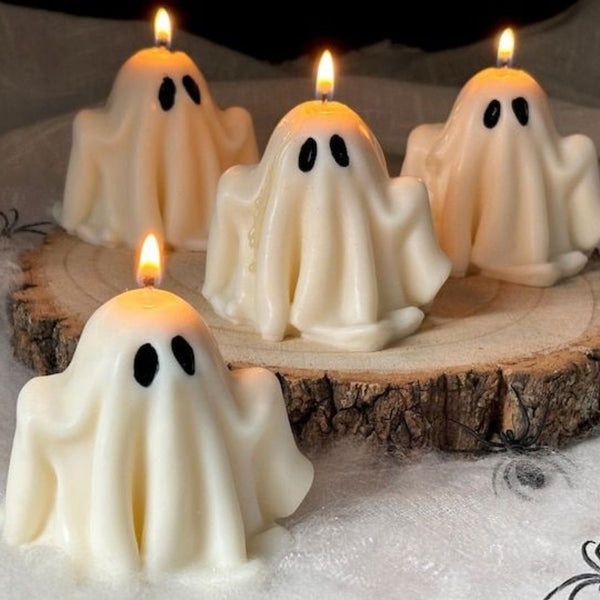 Four small white candles shaped like ghosts with black oval eyes, lit and placed on a wooden surface.