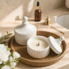 White ceramic candle jar with vertical stripes and round lid knob on woven tray.