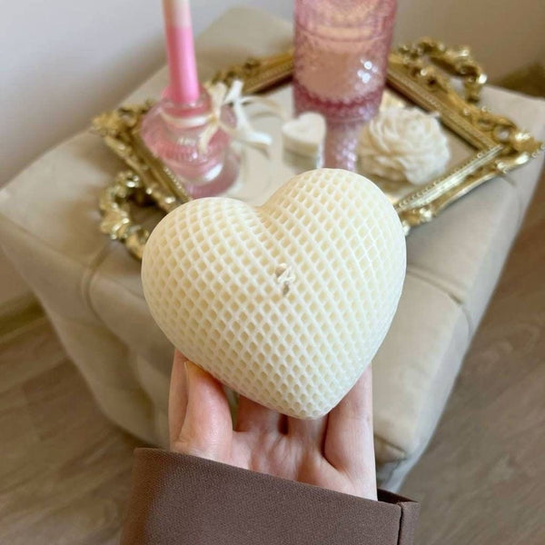 Creamy white heart-shaped candle with a textured waffle pattern held by hand.