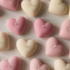 Pink and cream heart-shaped candles with textured surface arranged evenly on a beige background.