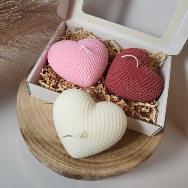Set of three heart-shaped candles in pink, red, and cream with textured surface in an open gift box.