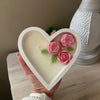 Heart-shaped white ceramic candle with three pink rose decorations and green leaves inside.