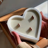White heart-shaped ceramic jar candle with three wooden wicks held in hands.