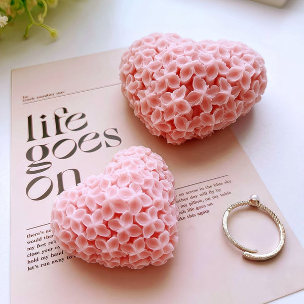 Pink heart-shaped candles covered in intricate floral patterns placed on a printed paper surface.