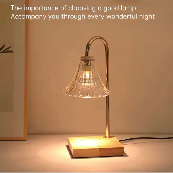 Electronic candle warmer lamp with curved brass arm and ribbed glass shade on wooden base.