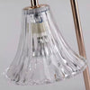 Clear ribbed glass lampshade with flared scalloped edge on metallic rose gold lamp arm.