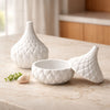 White ceramic jar with textured diamond pattern and matching lid on marble countertop.