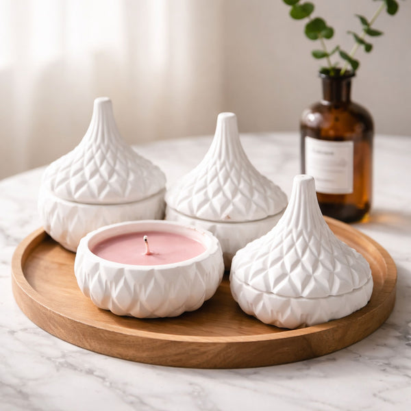 Set of three white ceramic jars with quilted pattern and conical lids, plus a pink candle dish, all on a round wooden tray.