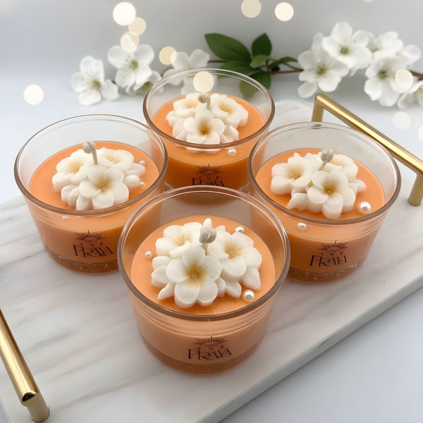 Set of four orange blossom jar candles with white flower-shaped wax toppers in clear glass holders on a marble tray.