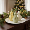 Set of three pastel snowman-shaped decorative candles in green, cream, and yellow on a white plate with festive pine and.