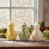 Set of three snowman candles in cream, green, and white with knit hats and scarves on wooden surface.