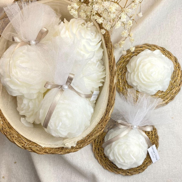 White peony flower scented candles wrapped in sheer white bags with silver ribbons, displayed in woven baskets.