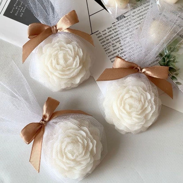 Small round white candle with detailed peony flower design, wrapped in sheer white fabric and tied with a bronze satin bow.
