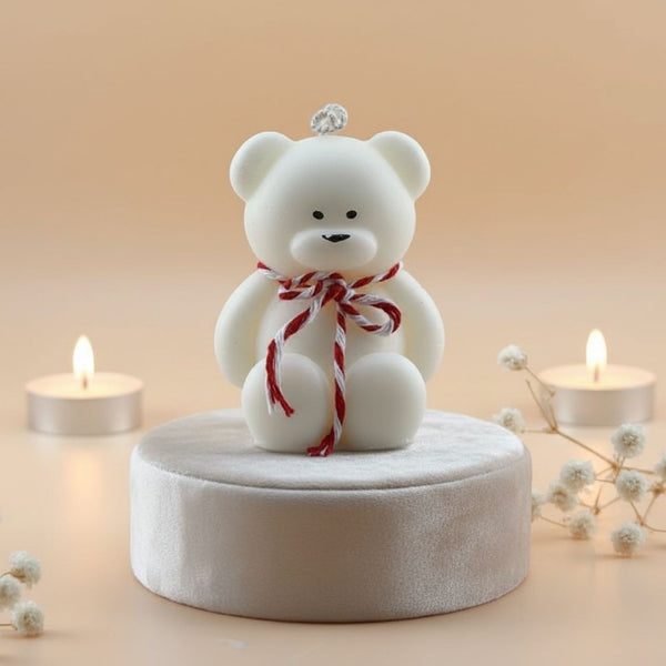 White teddy bear with a red ribbon on a beige background with candles and flowers.