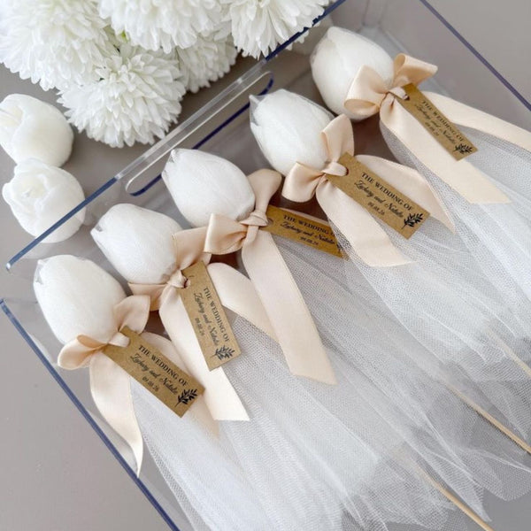 Set of five white tulip-shaped candles with beige bows and attached tags in transparent box.
