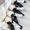 Set of five white tulip-shaped candles wrapped in sheer fabric with black ribbon and customizable tags.