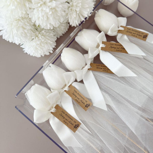 Five white tulip-shaped candles with white ribbons and brown tags in clear packaging.