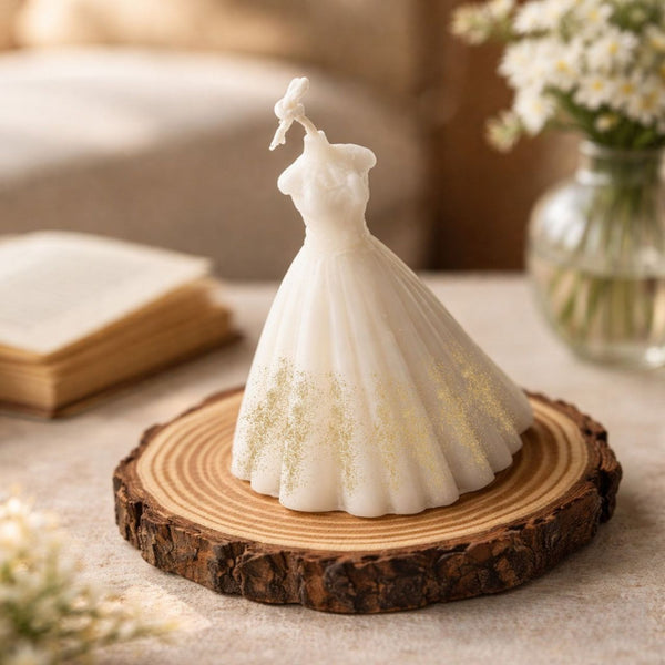 White bridal wedding dress-shaped candle with gold detailing, displayed on a wooden slice.