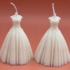 White bridal wedding dress-shaped candle with detailed bodice and flowing skirt against a peach background.