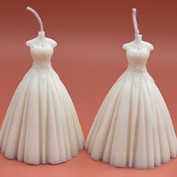 White bridal wedding dress-shaped candle with detailed bodice and flowing skirt against a peach background.