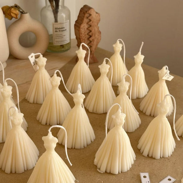 Set of cream bridal wedding dress candles with pleated skirt details on a wooden surface.